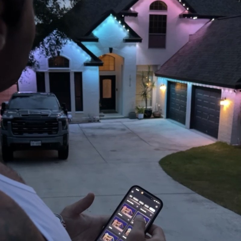 Dazzl team member showing a homeowner the scene-switching app with a permanent lighting installation in the background