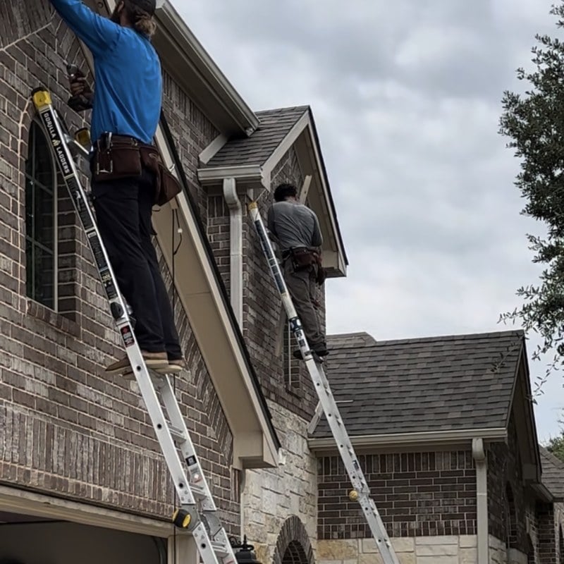 Two Dazzl installers on ladders mounting permanent LED channel under the soffit of a Texas home.