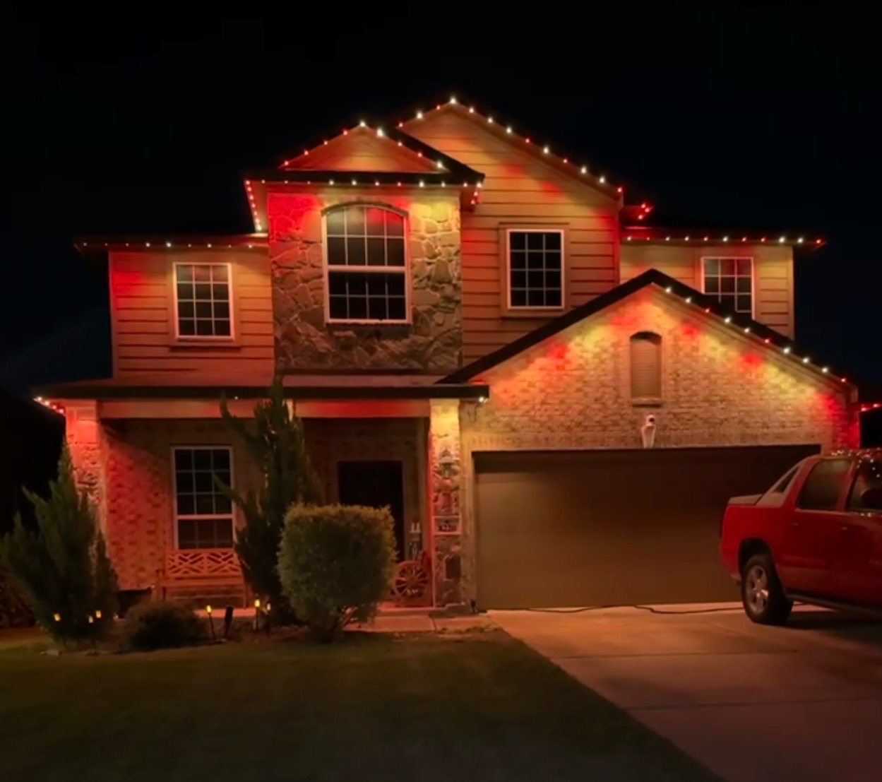 Texas stone-and-siding two-story home with red and warm white permanent LED holiday lighting